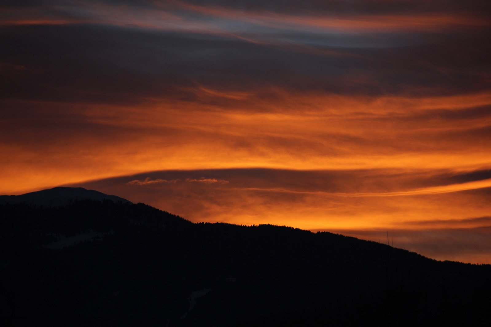 the silhouette of a mountain against an orange sunset sky