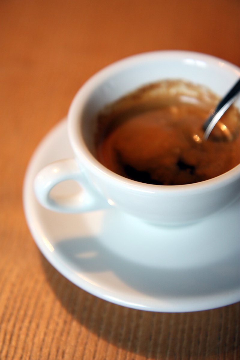 a small white cup full of coffee next to a spoon