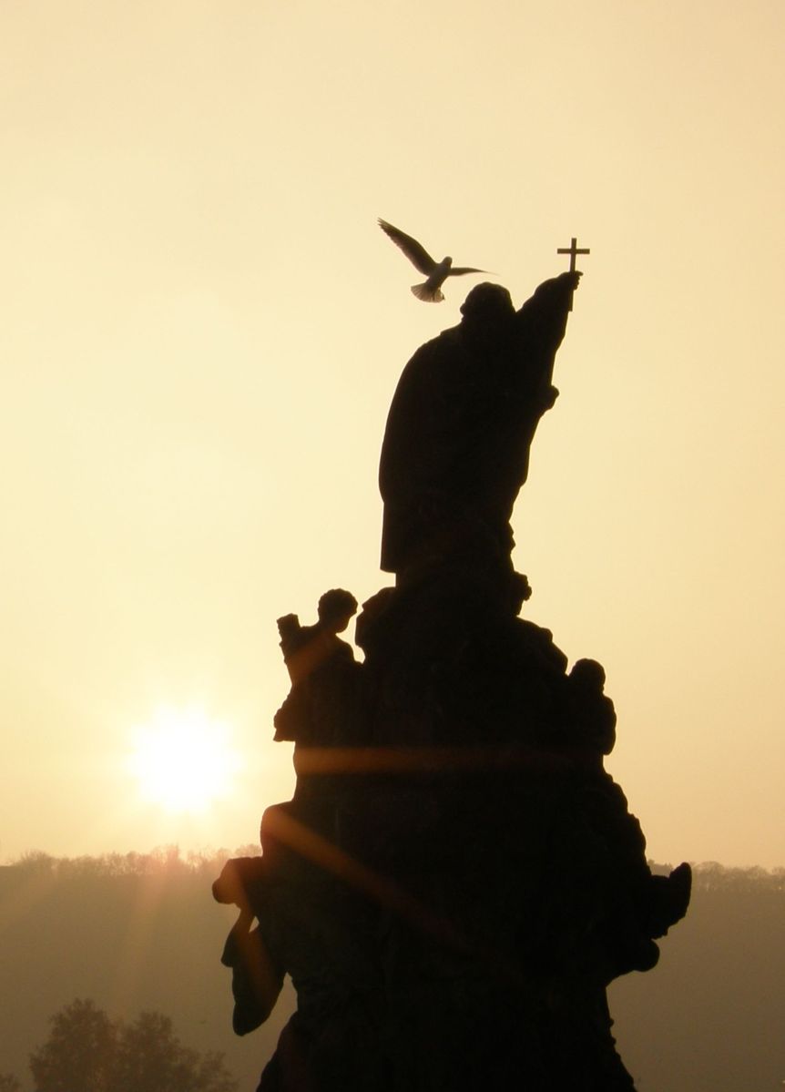 a bird flying above the statue at sunset