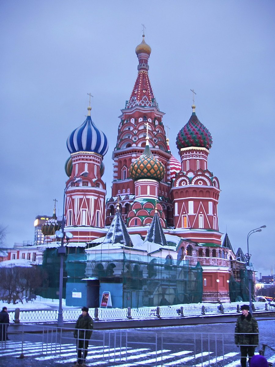 an ornate red building surrounded by trees on top of snow covered ground