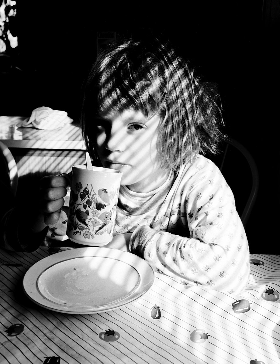 a little girl sitting at a table eating and drinking out of a cup
