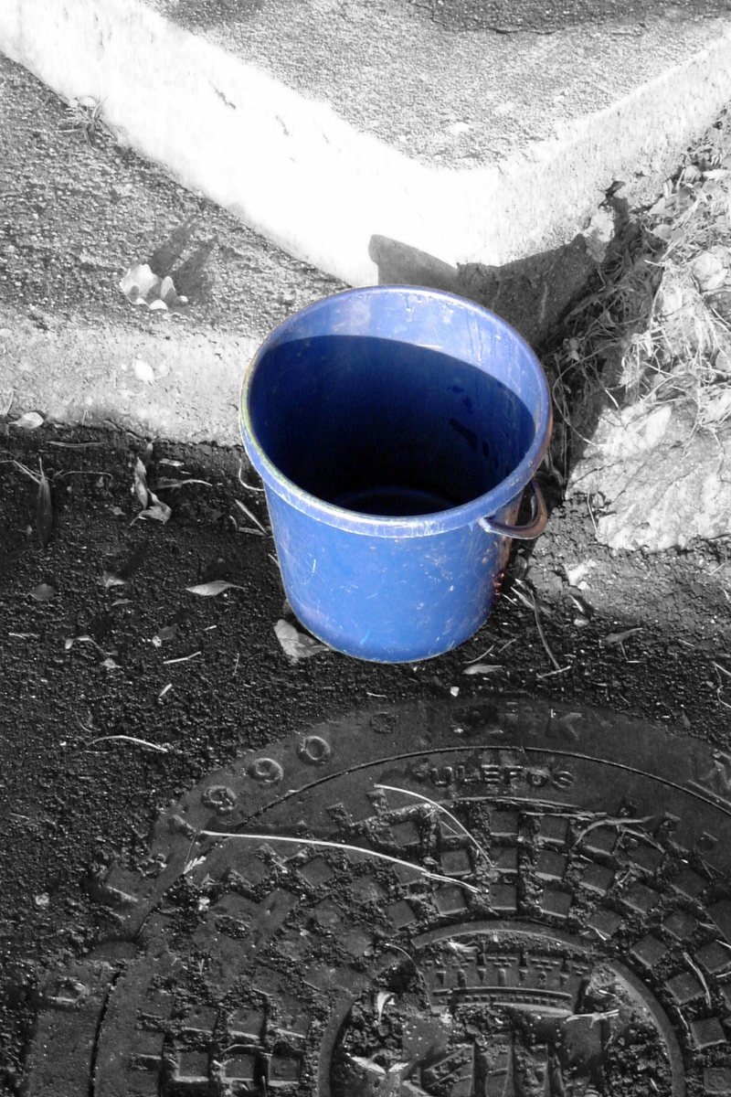 a blue bucket sitting in the mud on a sidewalk