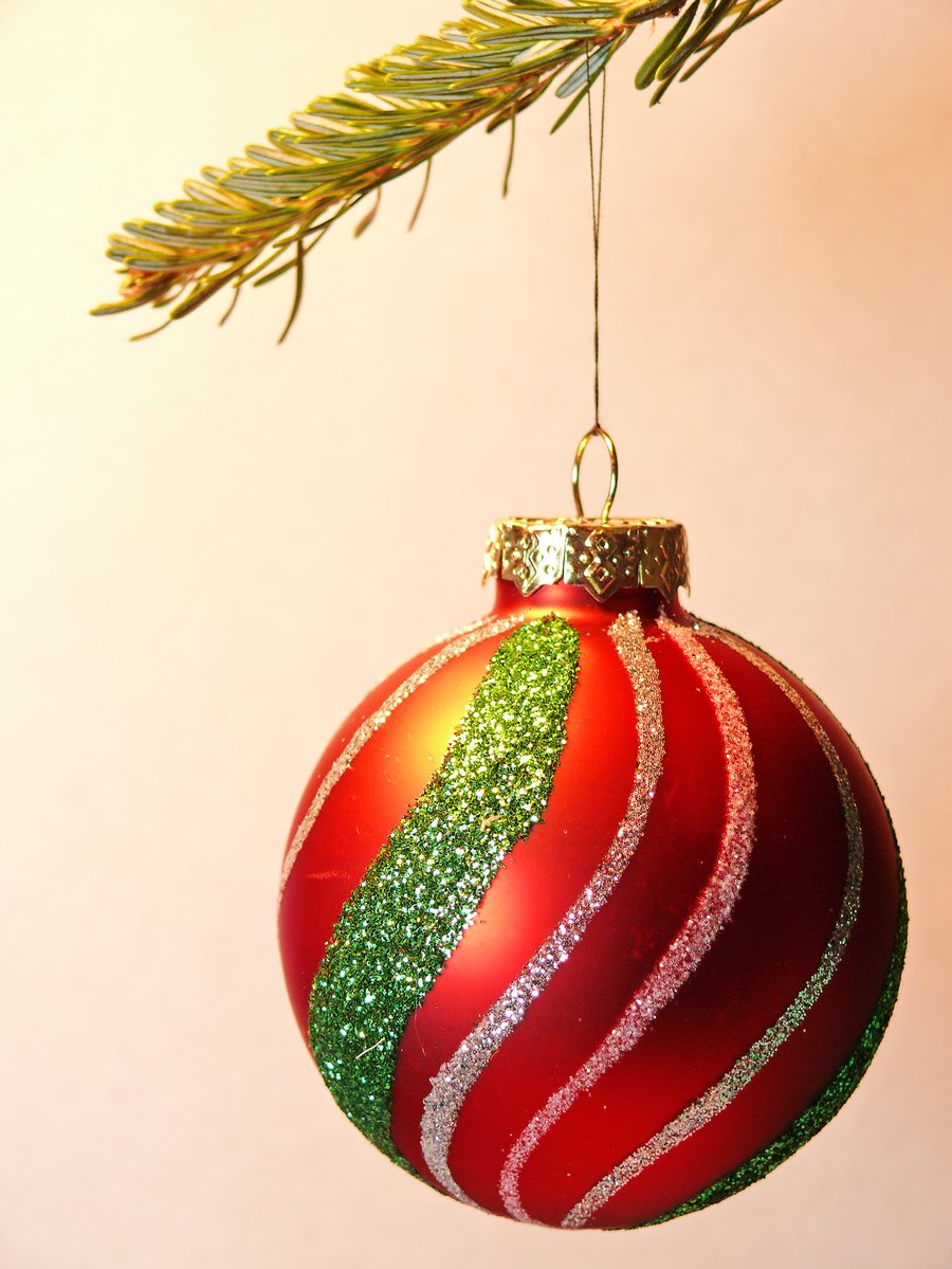 a red christmas bauble hanging from a pine tree