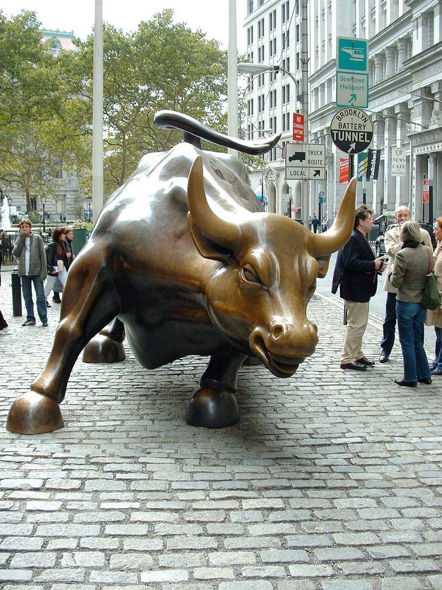 people standing around a bronze bull statue in the middle of a busy city