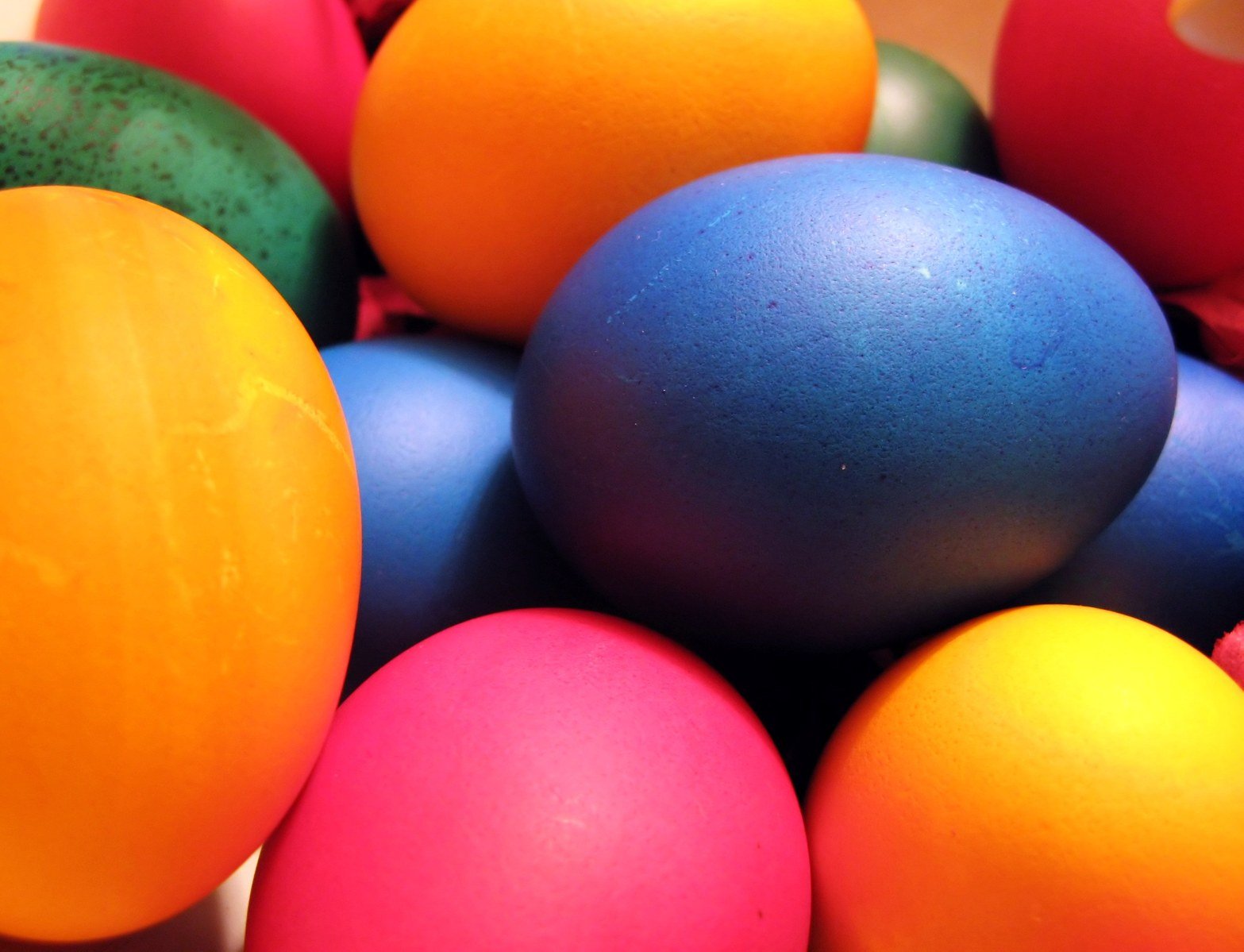 several different colored eggs with a green apple in the background