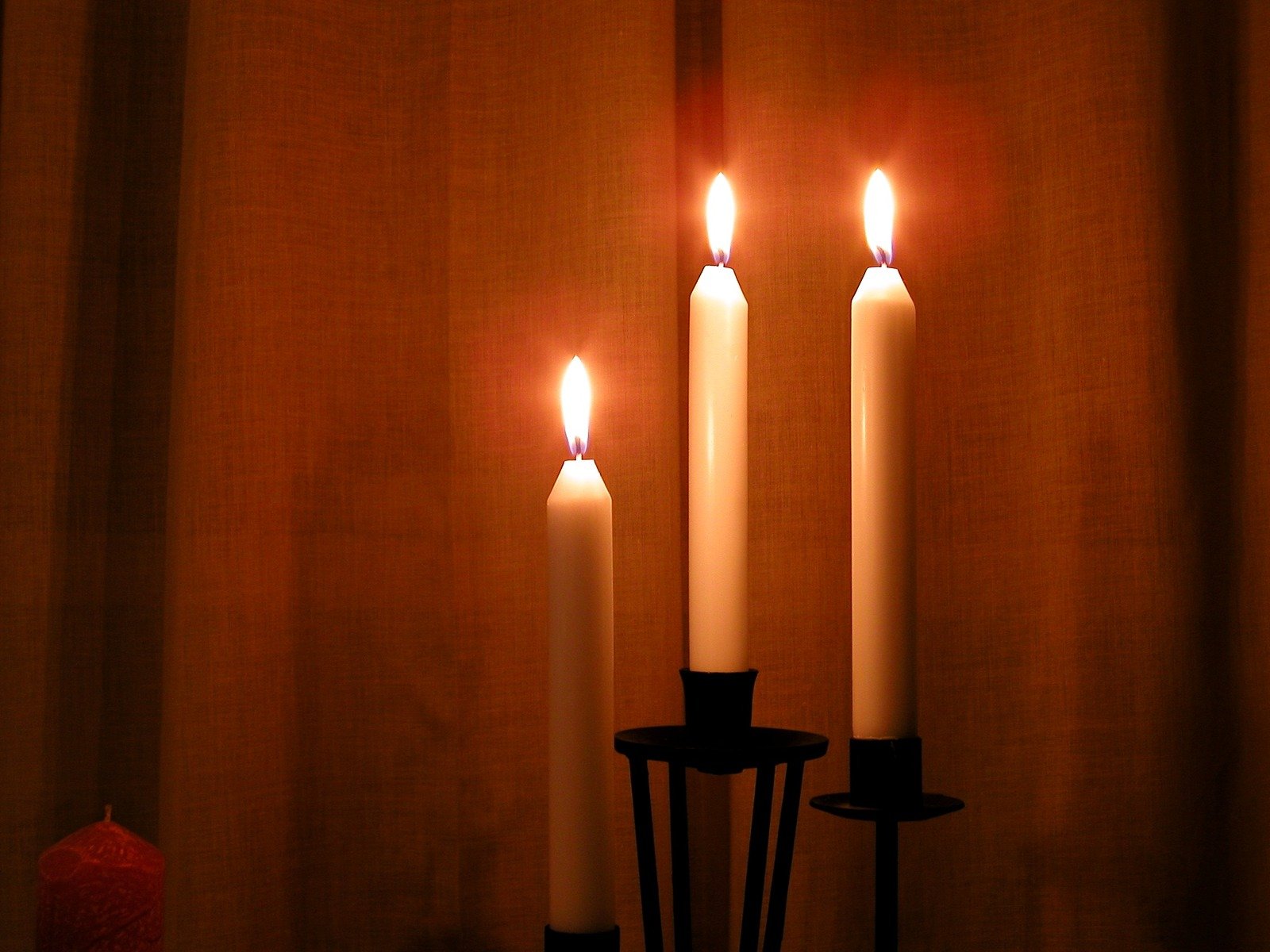 three lit candles sit in front of a curtain