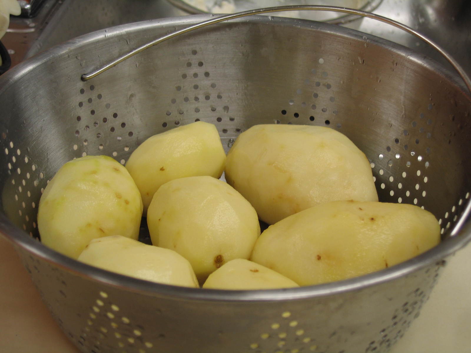 there is a metal bowl with some potatoes in it