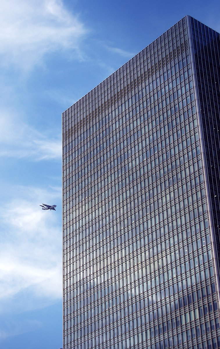 a plane flying by near a glass building