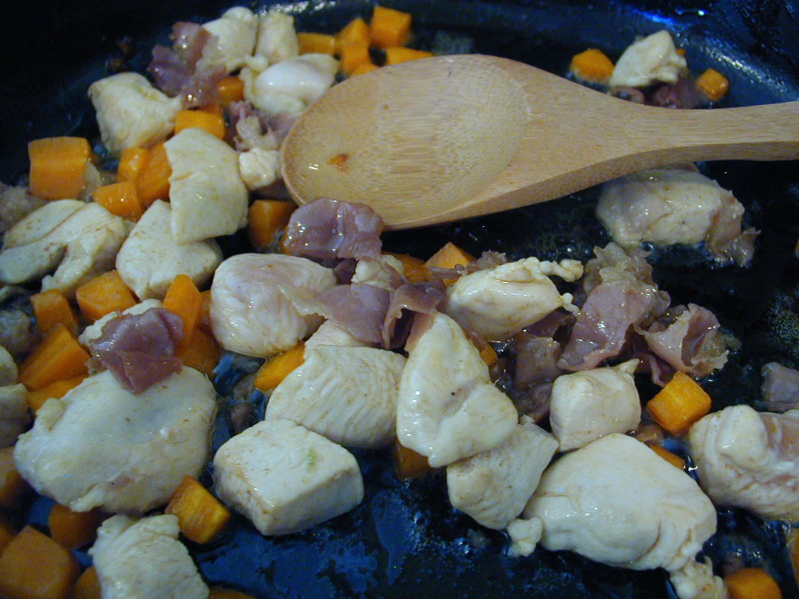 chicken, carrots and meat cooking in a pan with a wooden spoon