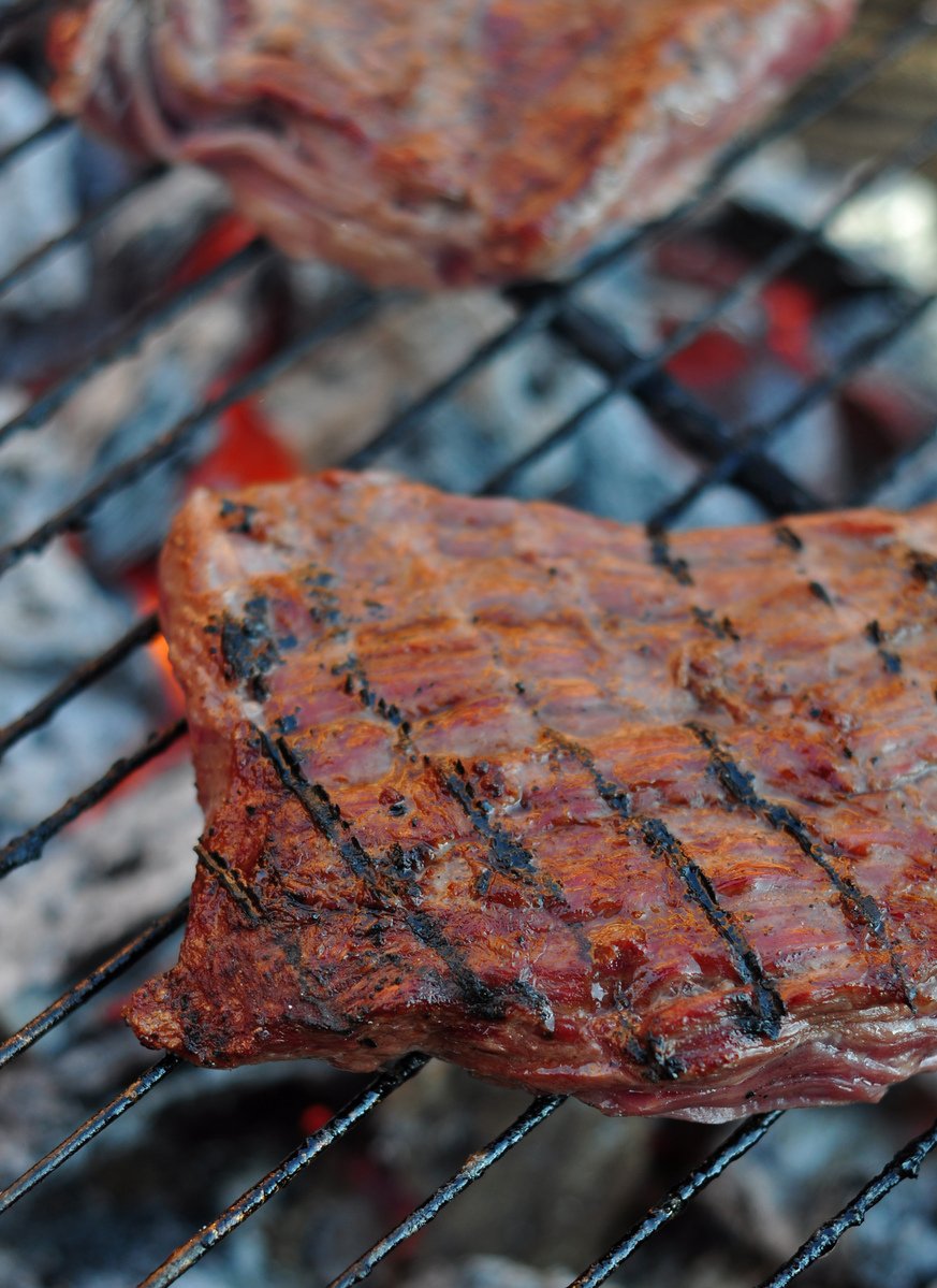 two pieces of steak cooking on a grill