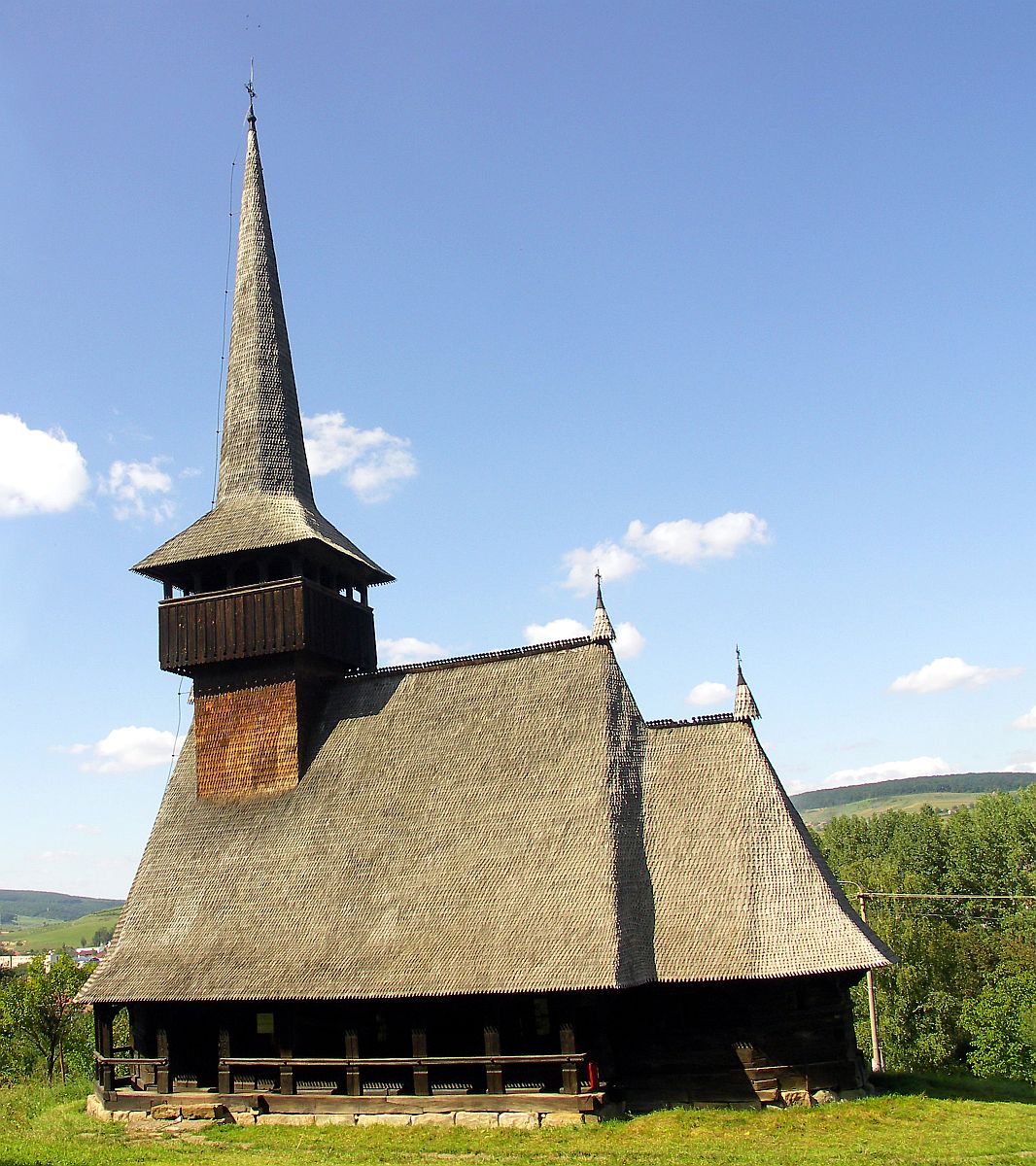 a tall wooden church with a steeple on a grassy hillside