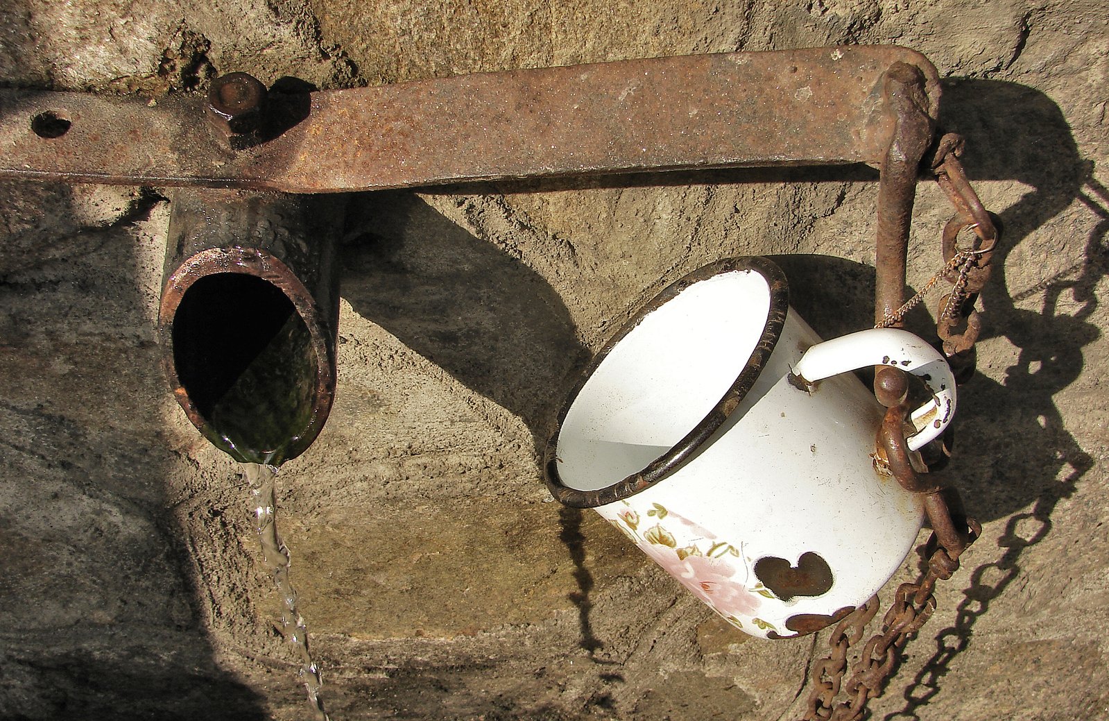 an old chain hung around an iron railing holding a broken white mug