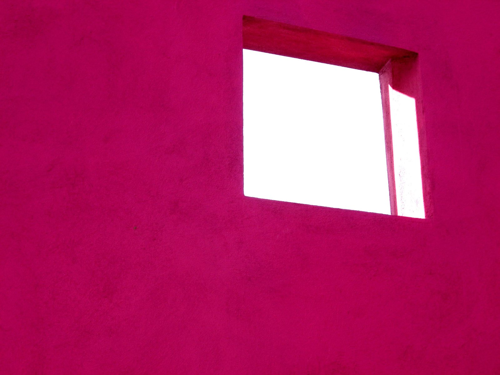 a bright red wall with a window reflecting it's light