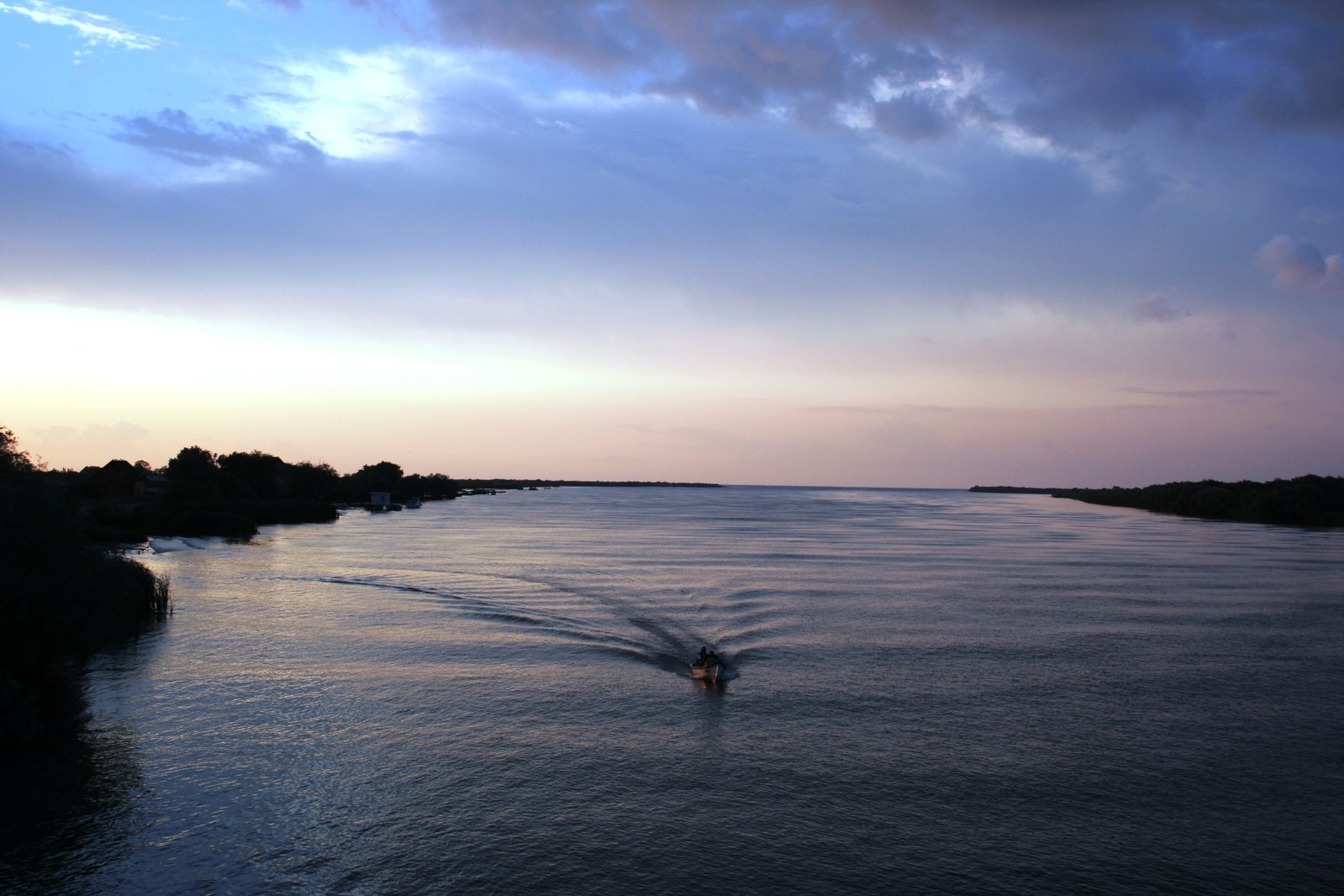 boat riding on river, at dusk with clouds overhead