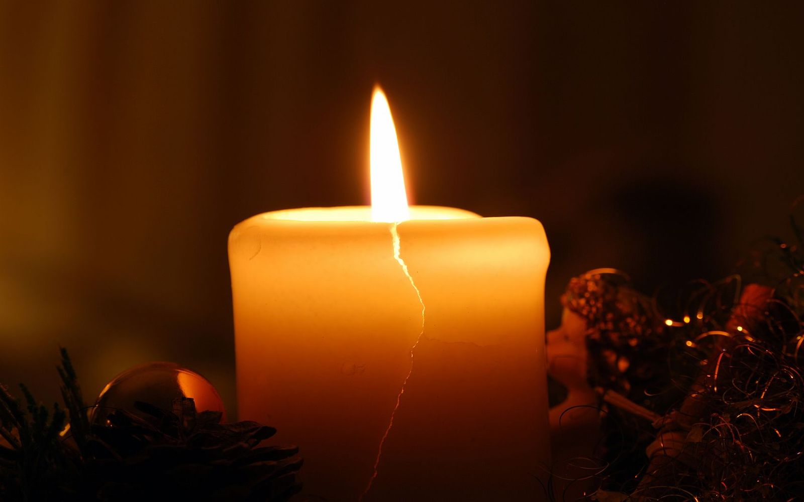 an illuminated candle with christmas ornaments on a table