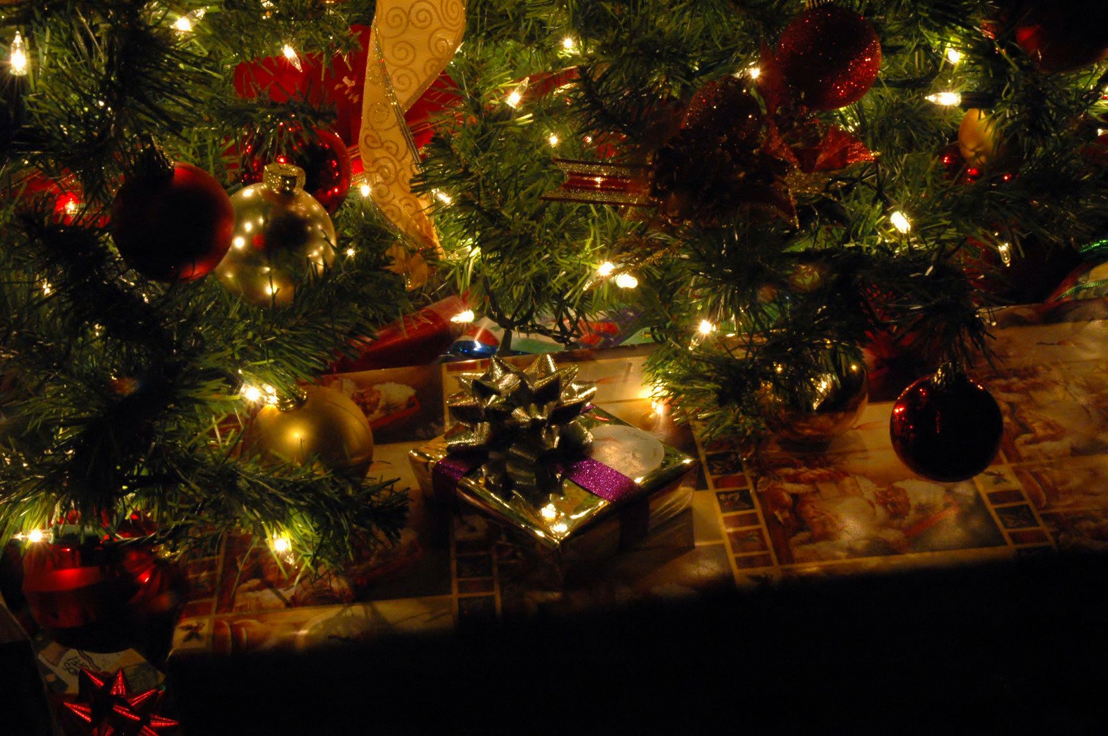 gifts underneath a lit christmas tree on a dark floor
