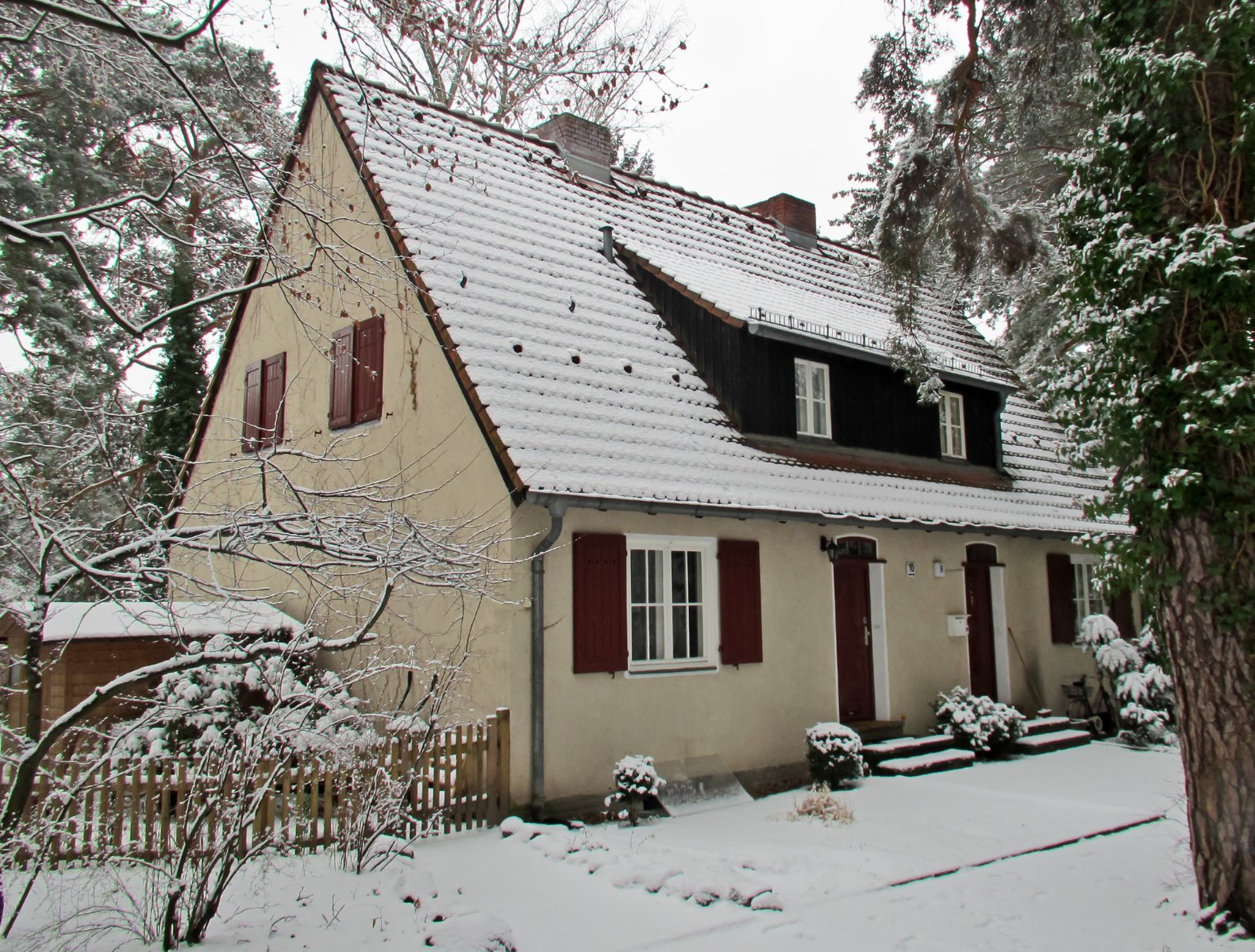 a snow covered house sits outside with red shutters