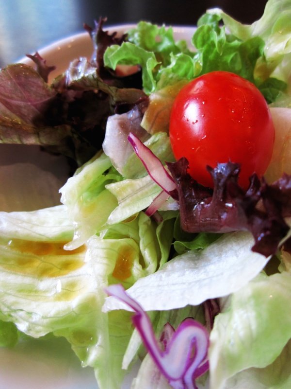 a tomato is sticking out of a salad with lettuce and radishes