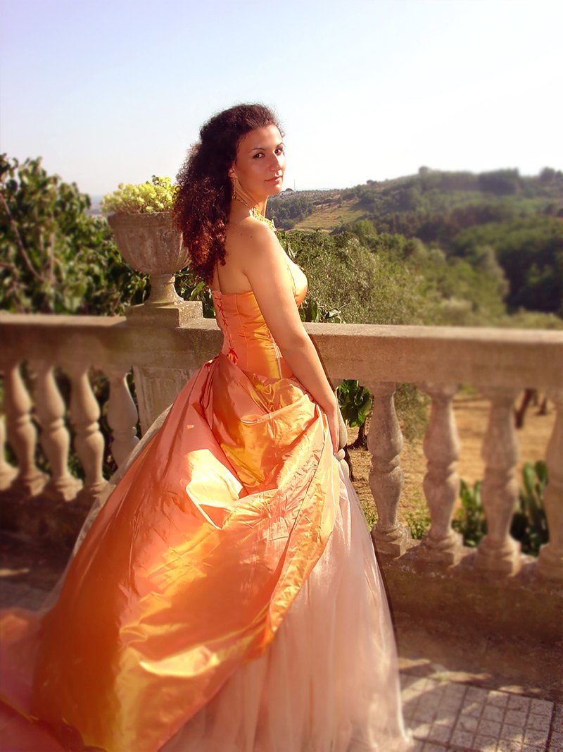 a girl in a orange and pink dress stands on a balcony
