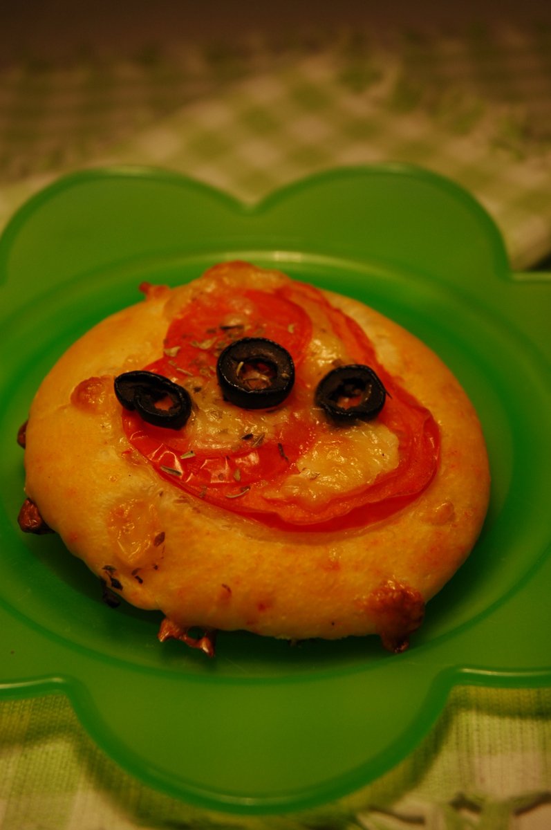 the mini pizza has a face made out of olives and pepperoni