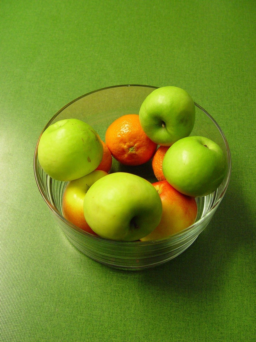 a glass bowl filled with lots of fruit on top of a green table