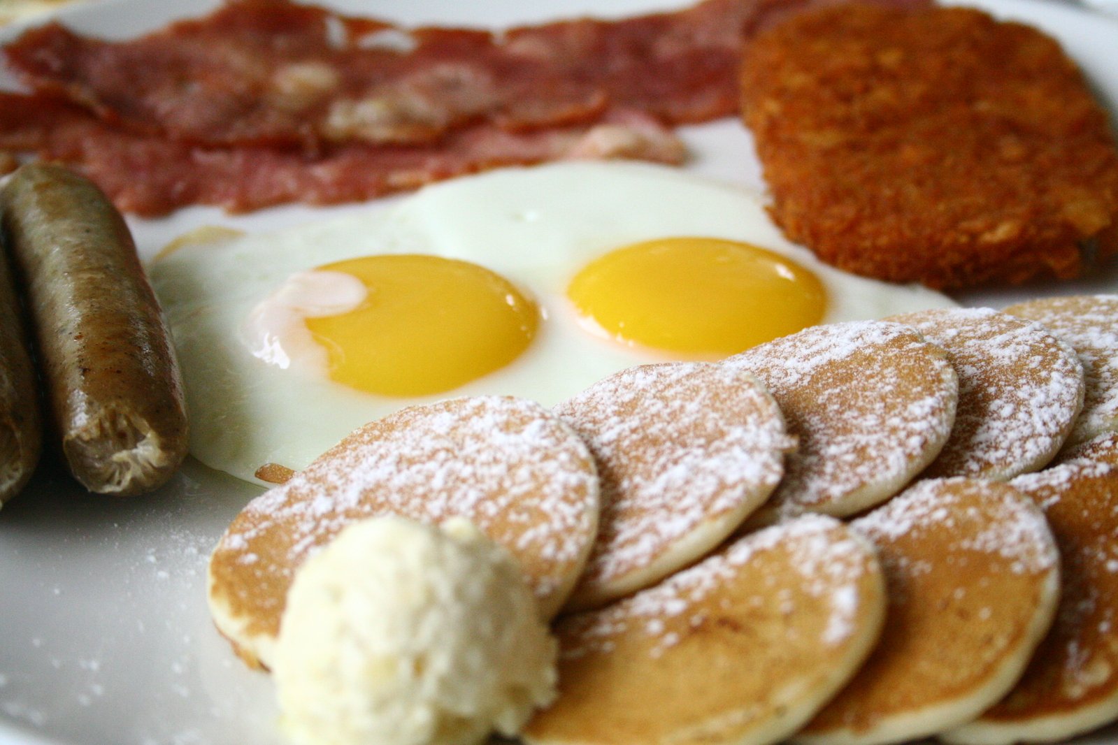 a plate full of pancakes and sausages, eggs, sausage and potatoes