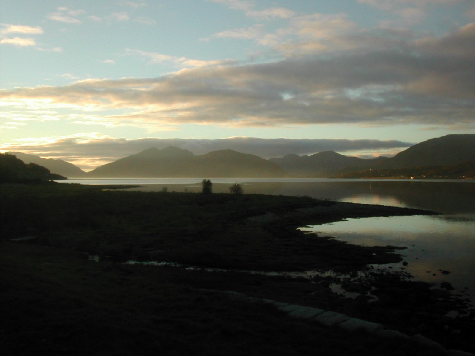 a body of water next to a shore with a mountain range in the background