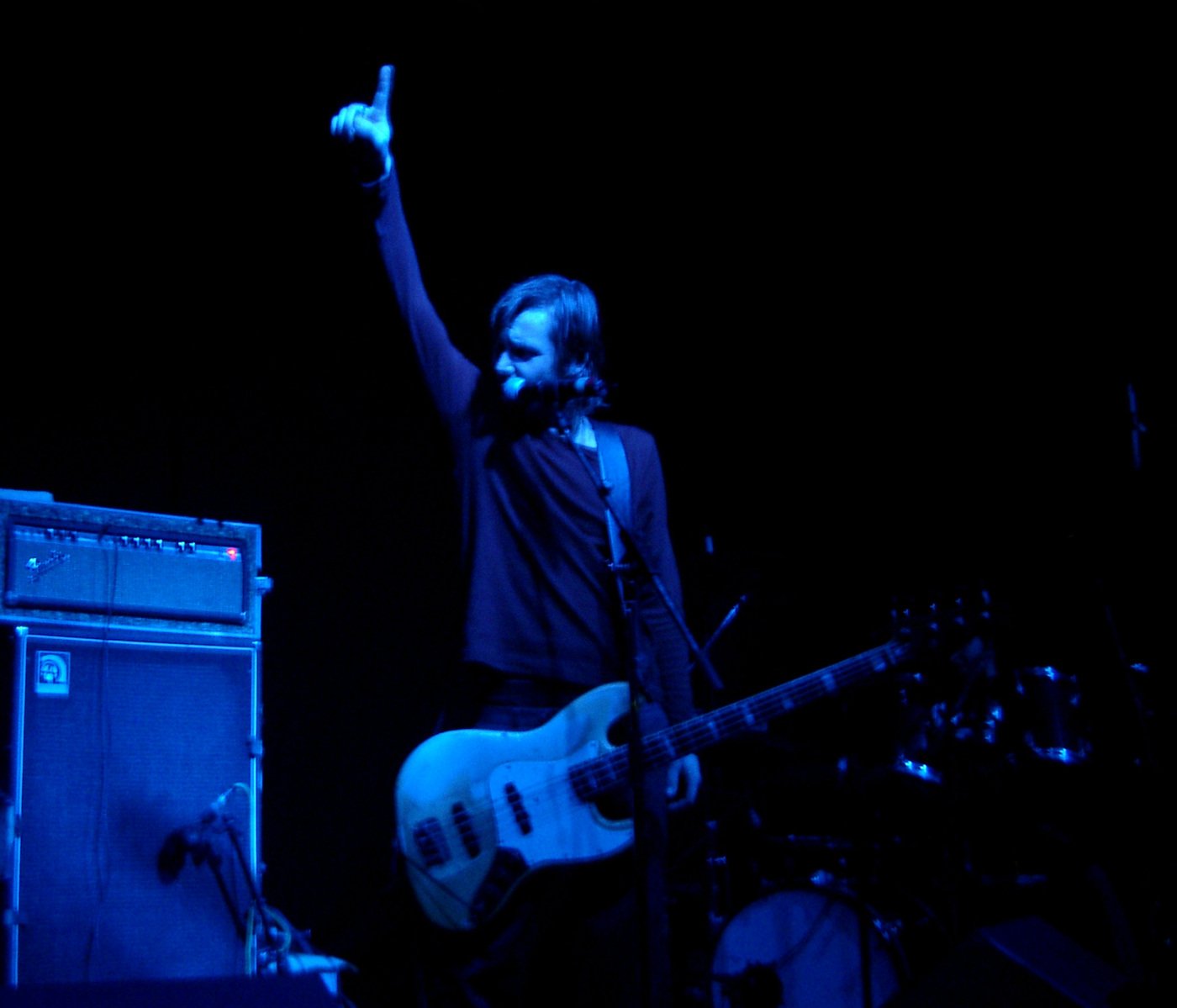 a man in black standing at a microphone with his arm up