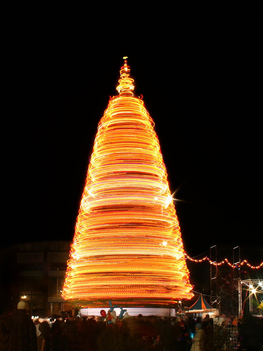 lighted christmas tree on the street with several people around