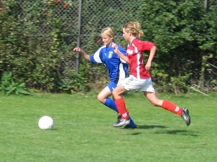 two girls playing soccer against each other in a grassy field