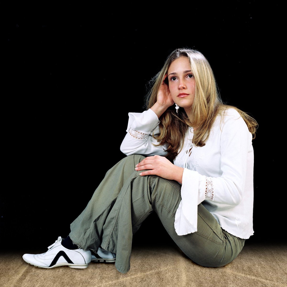 young woman with long hair sitting on floor, holding hand on her chin