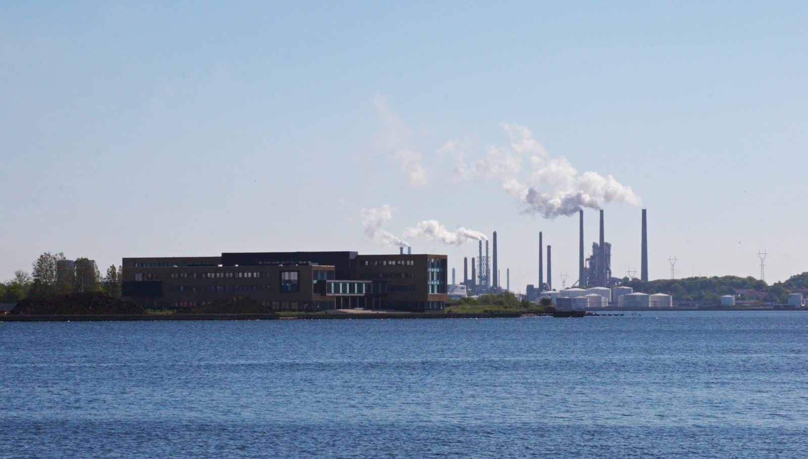 smoke pouring out of a chimney behind industrial buildings