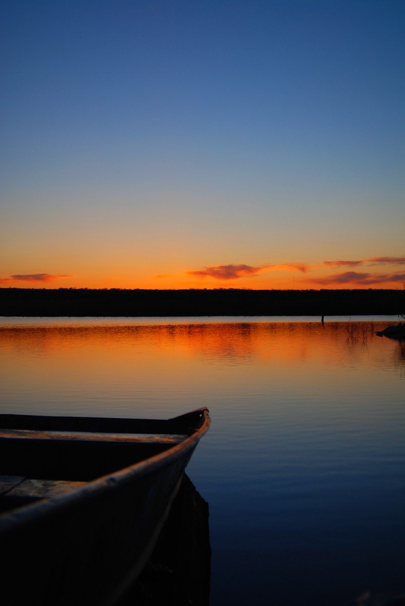 the sun rising over the water and a lone boat on the still lake