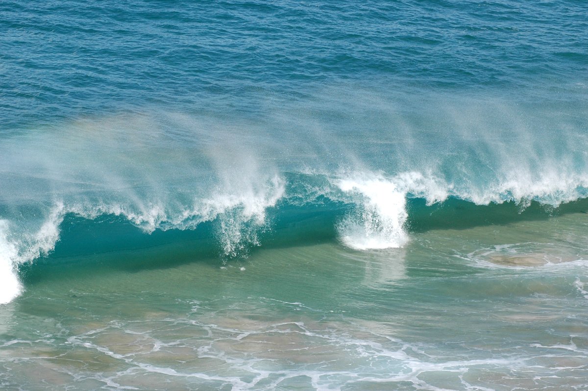 a huge wave hitting the shore with a plane in it