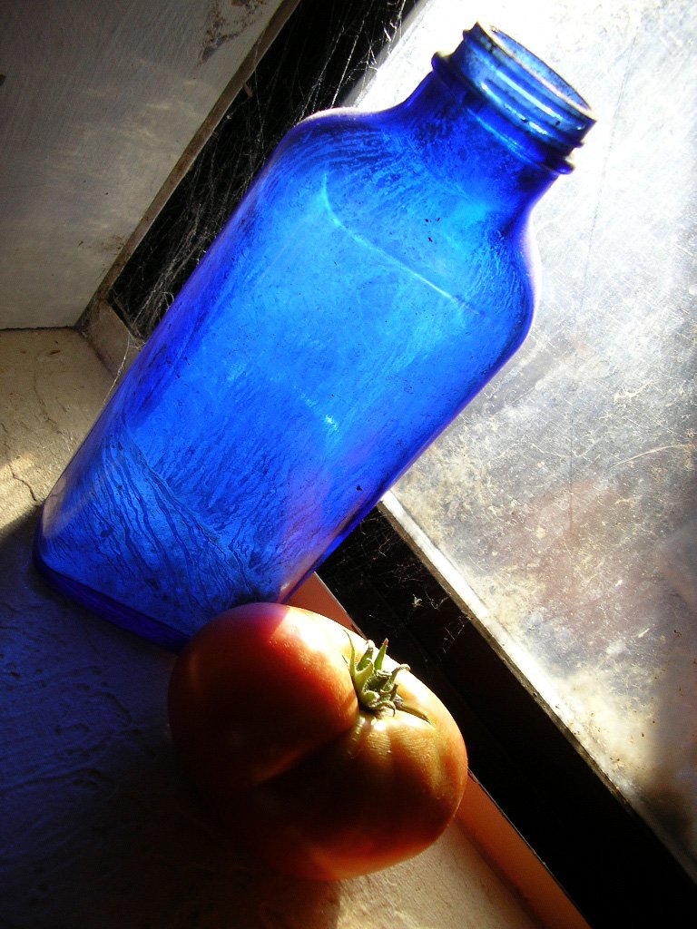 a hand holding an unpeeled blue glass bottle with a tomato in it