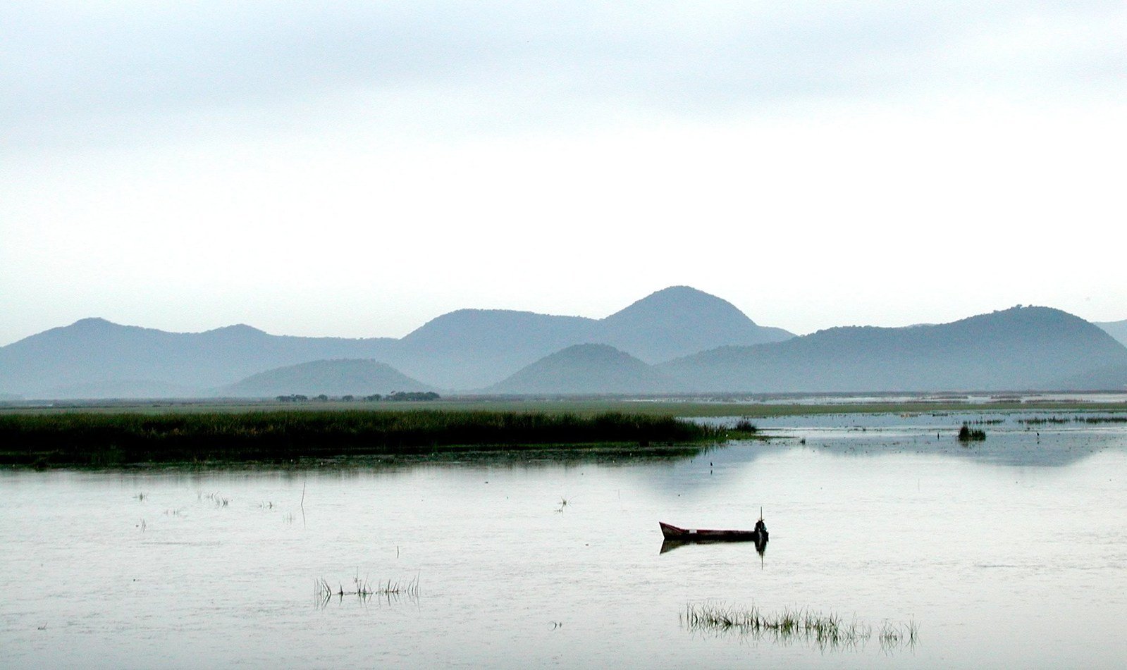 a boat is floating in some water with mountains behind it