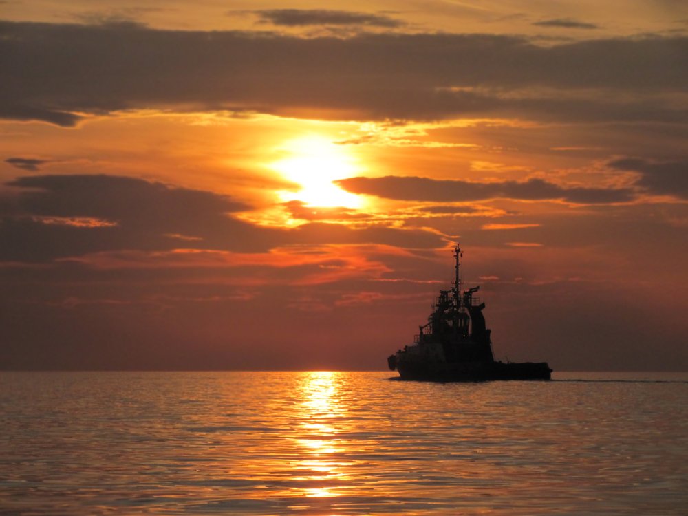 the silhouette of a small ship at sunset