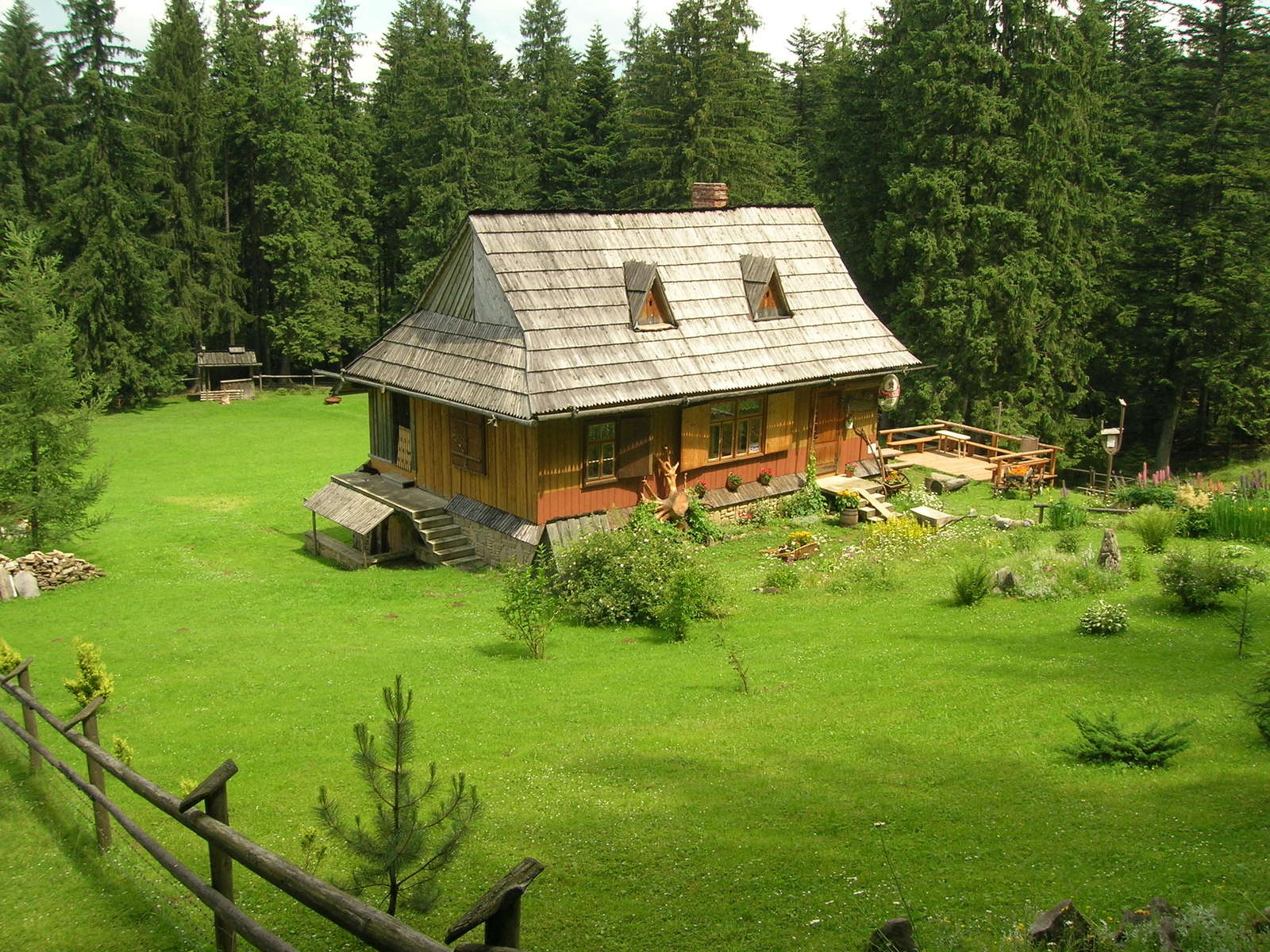 a small log cabin is seen in the green, grassy field