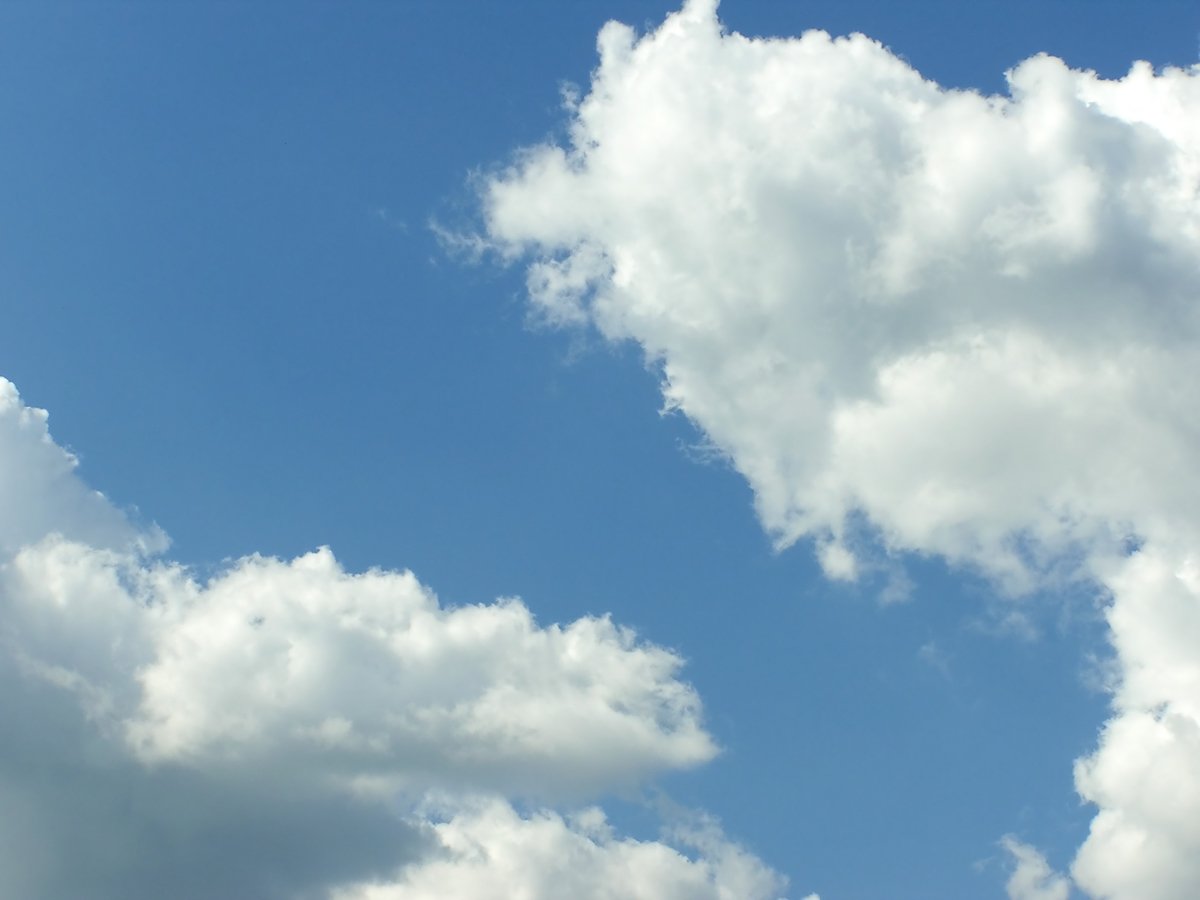 the sky is filled with puffy clouds and the plane flies overhead