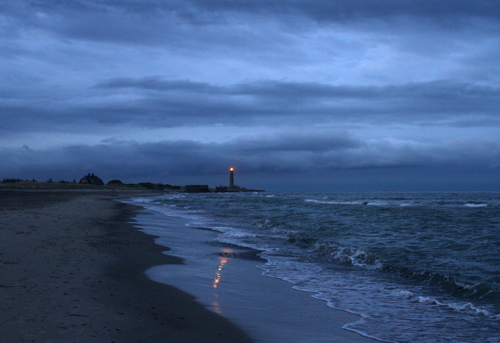 the waves are lapping on to a beach and a lighthouse is shown at night