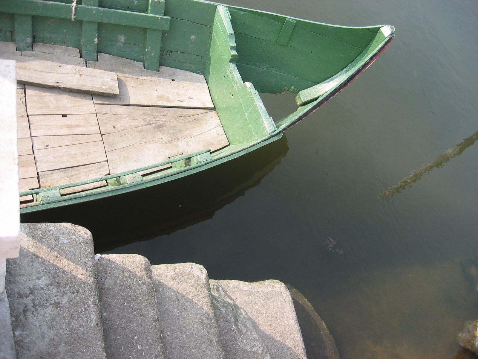 a small green boat on water next to concrete steps