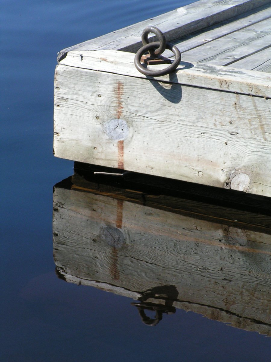 a wooden dock over looking blue water with a metal ring