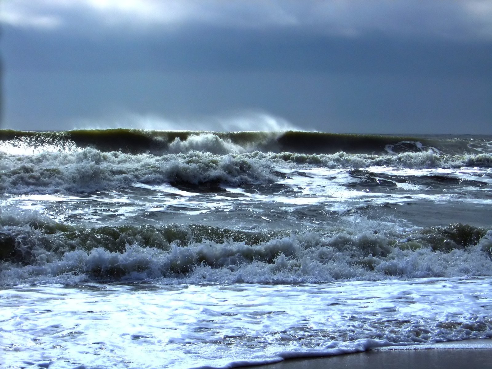 waves crashing on the shore under cloudy skies