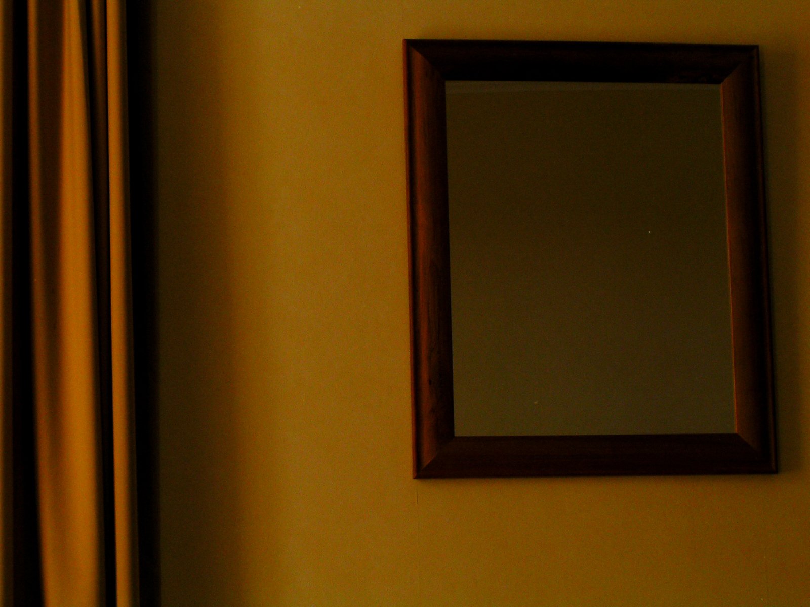 an old mirror hung on a yellow wall near the curtains