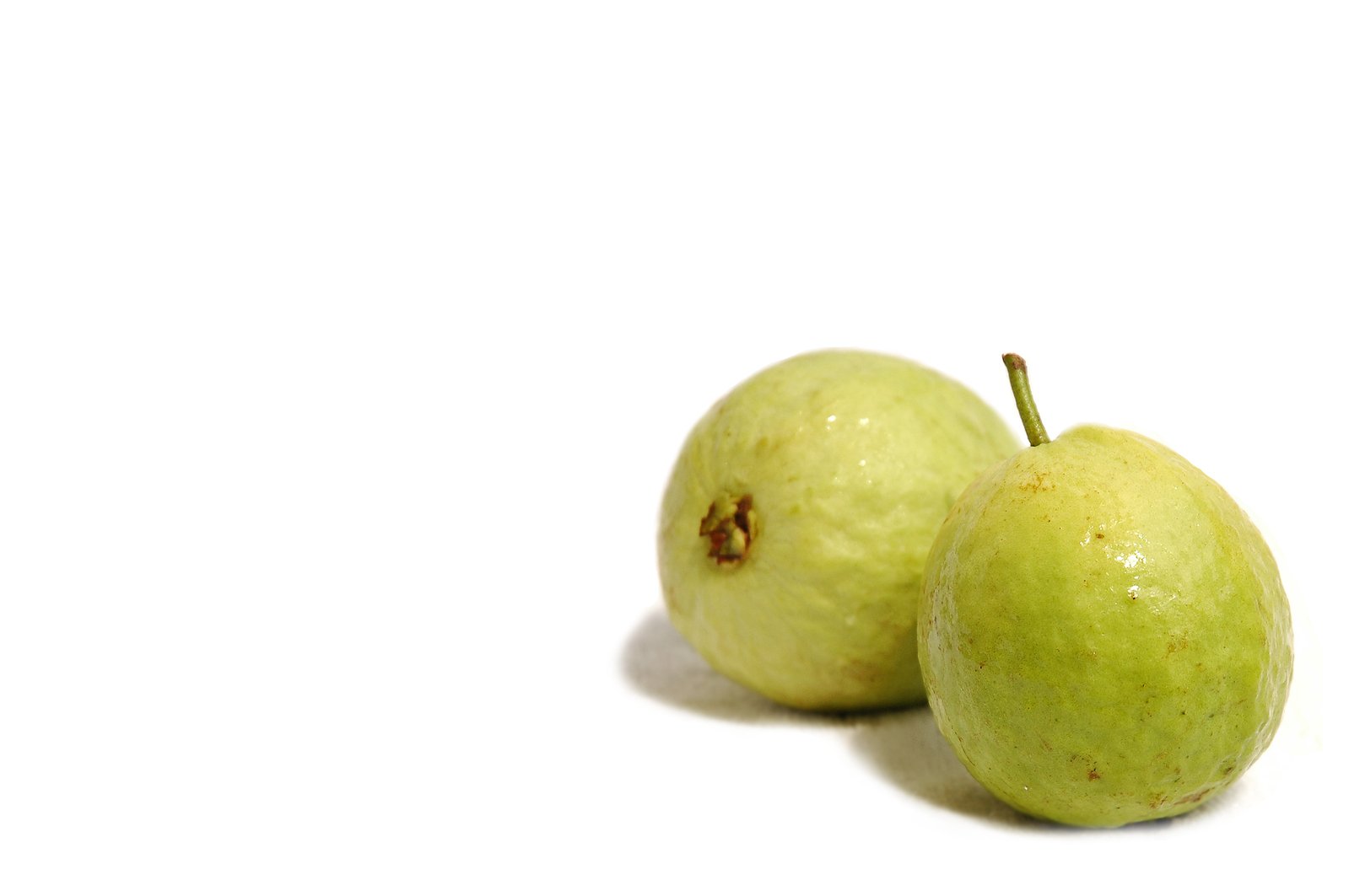 two green apples sitting on top of a white surface