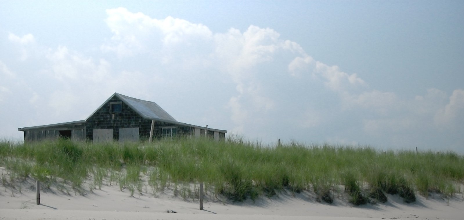 an old barn in a grassy field sits next to the beach