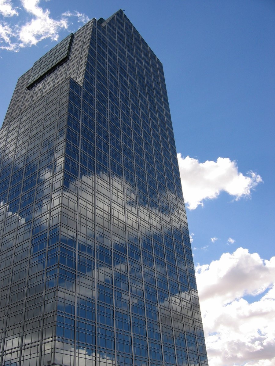 a tall building has a reflection of some clouds in the side