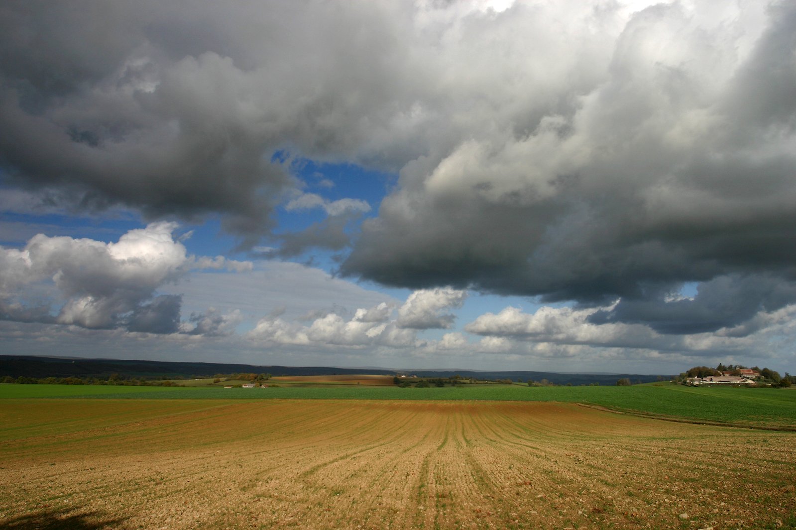 storm clouds hover over the countryside with a farm