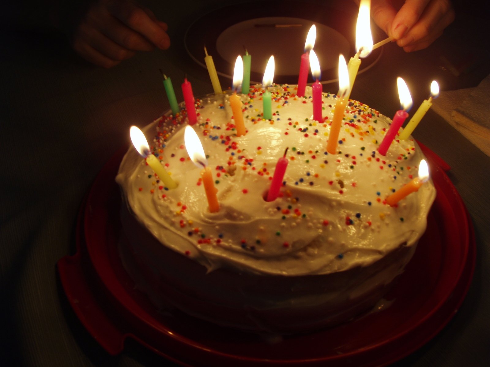 someone lighting candles on a birthday cake with white icing