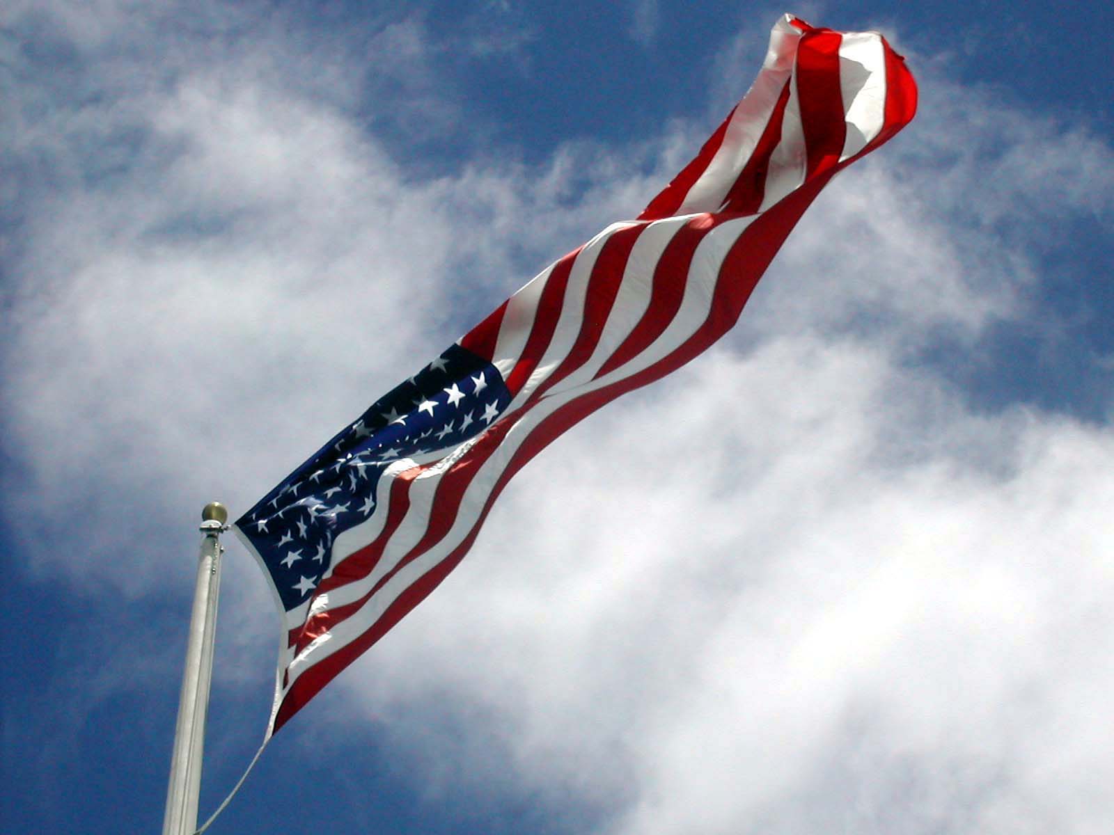 the american flag flies high on a bright, partly cloudy day